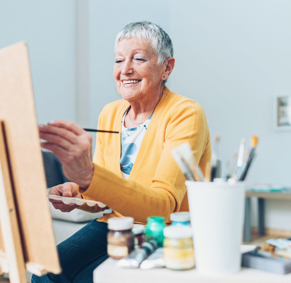 Woman smiling as she paints on a canvas.