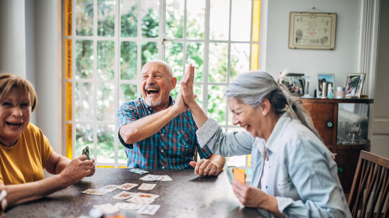 Seniors smiling and high-fiving as they play cards together.