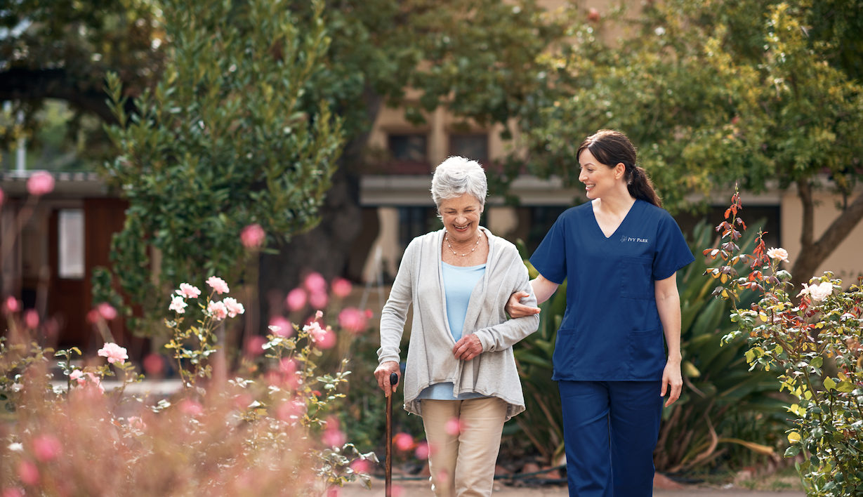 Elderly woman walking with nurse in garden