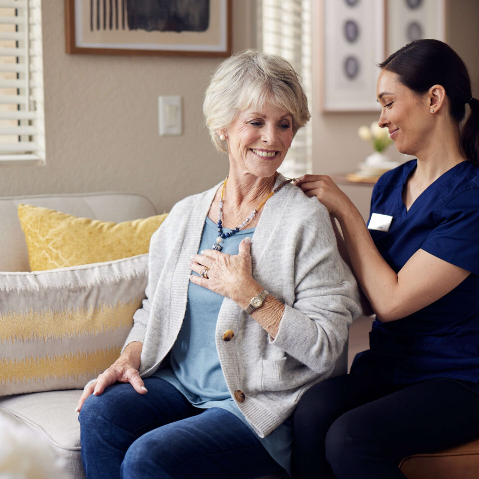 A caregiver helping an elderly woman put on her necklace.