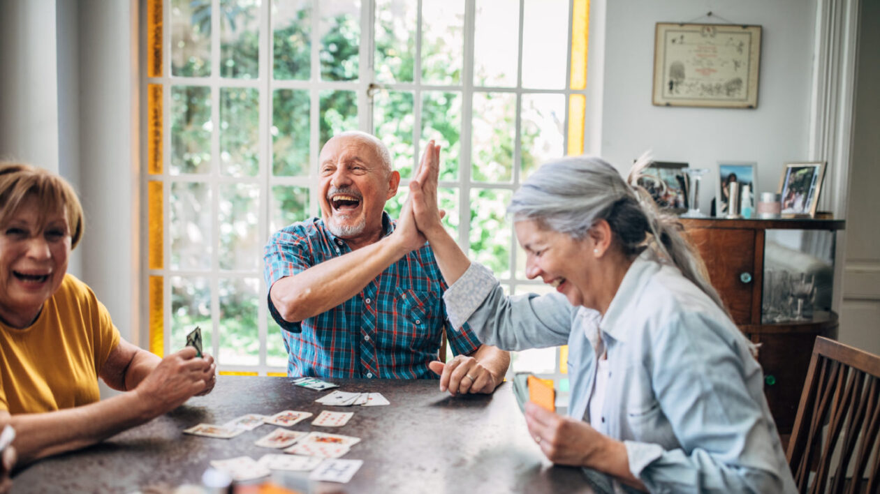 Seniors smiling and high-fiving as they play cards together.