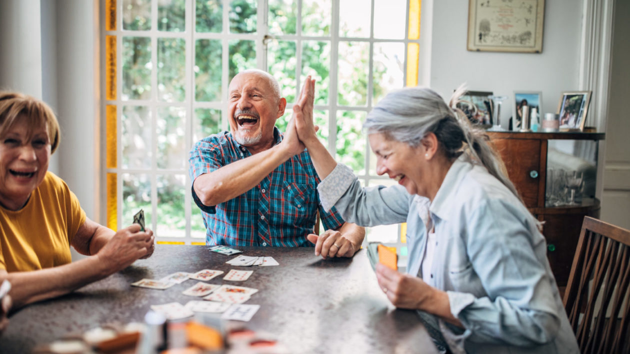 Seniors smiling and high-fiving as they play cards together.