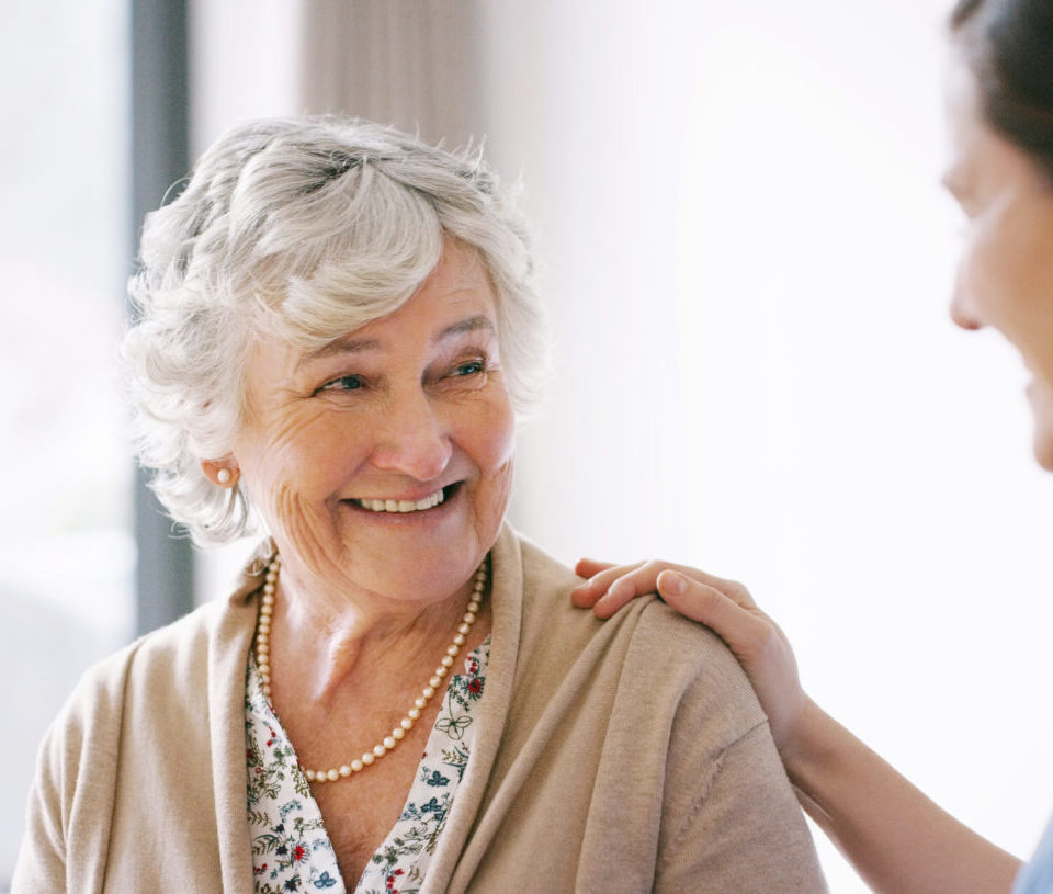 Senior woman smiling at a caregiver, with her hand on her shoulder.