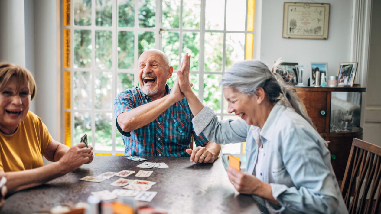 Seniors smiling and high-fiving as they play cards together.