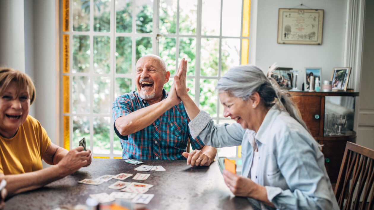 Seniors smiling and high-fiving as they play cards together.