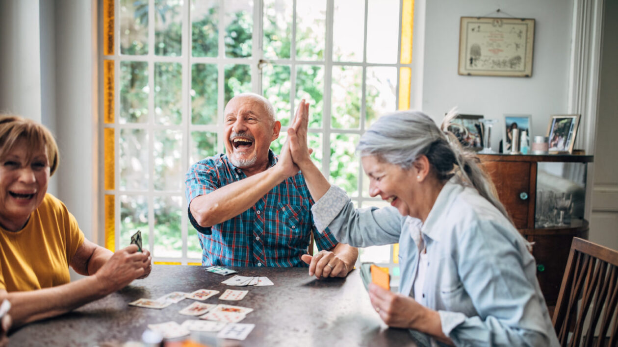 Seniors smiling and high-fiving as they play cards together.