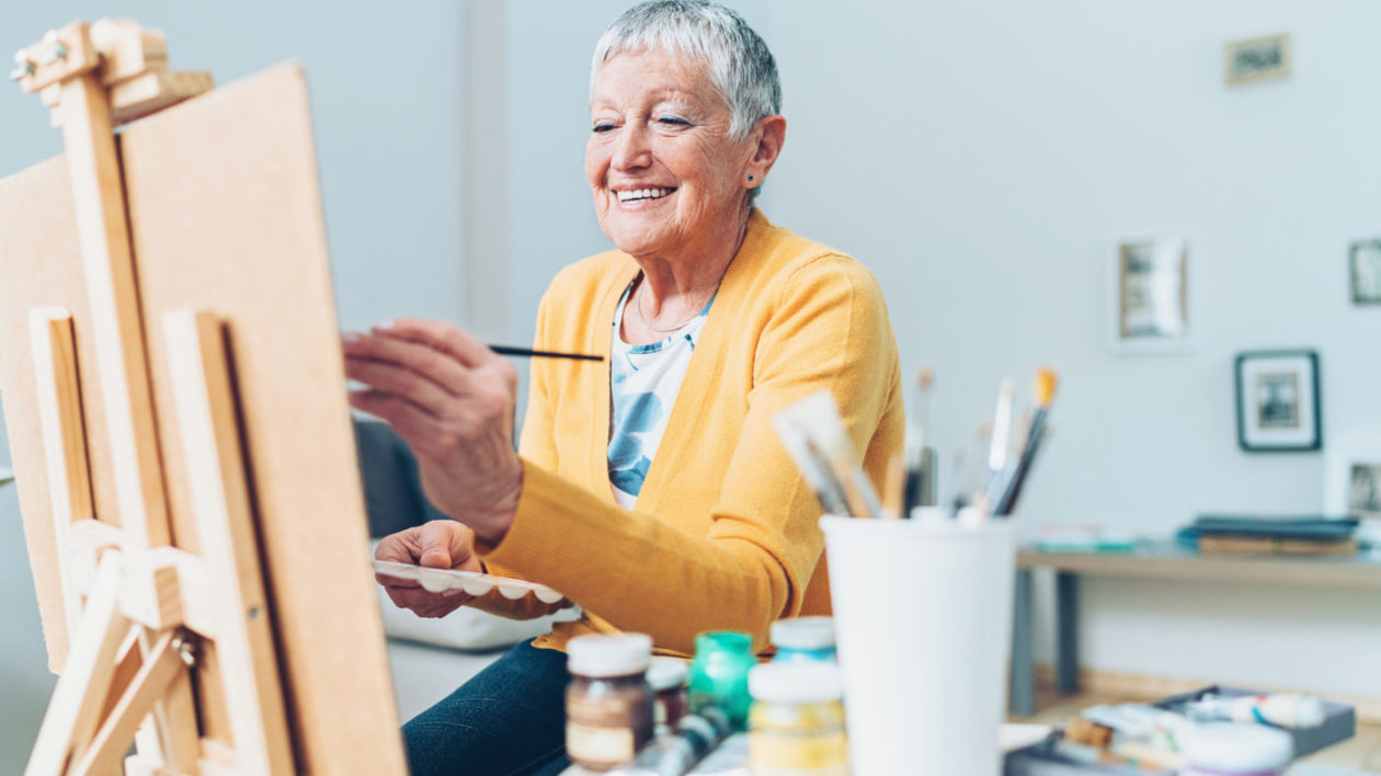Woman smiling as she paints on a canvas.
