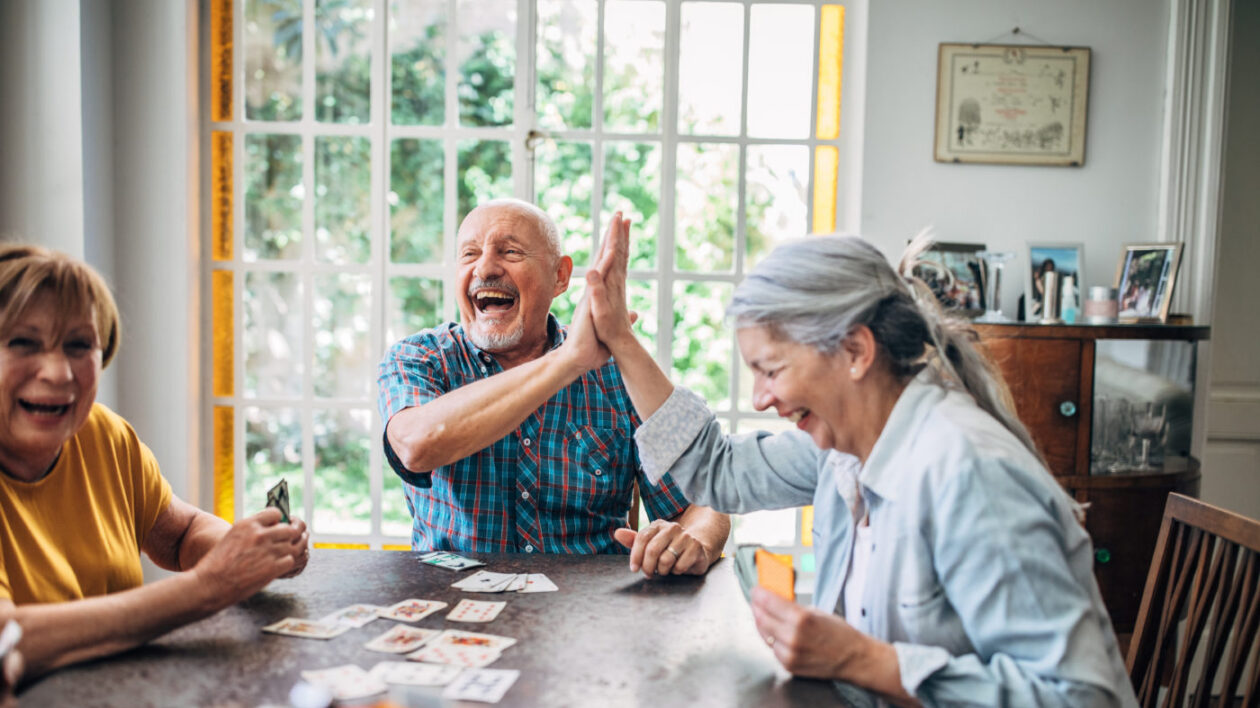 Seniors smiling and high-fiving as they play cards together.