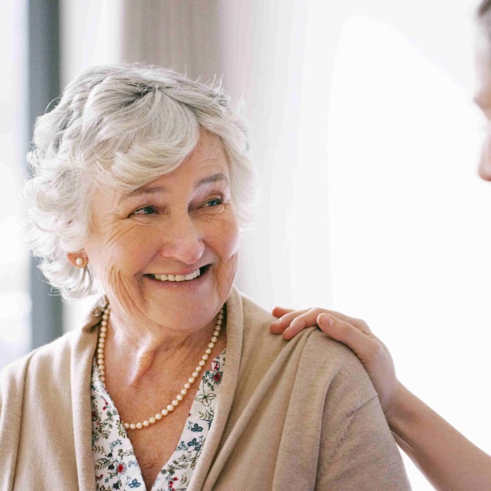 Senior woman smiling at a caregiver, with her hand on her shoulder