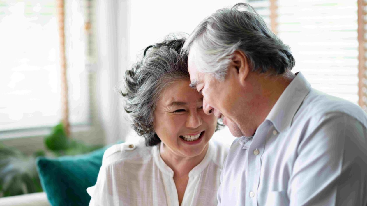 An older couple smiling and laughing, sitting close and enjoying each other's company.