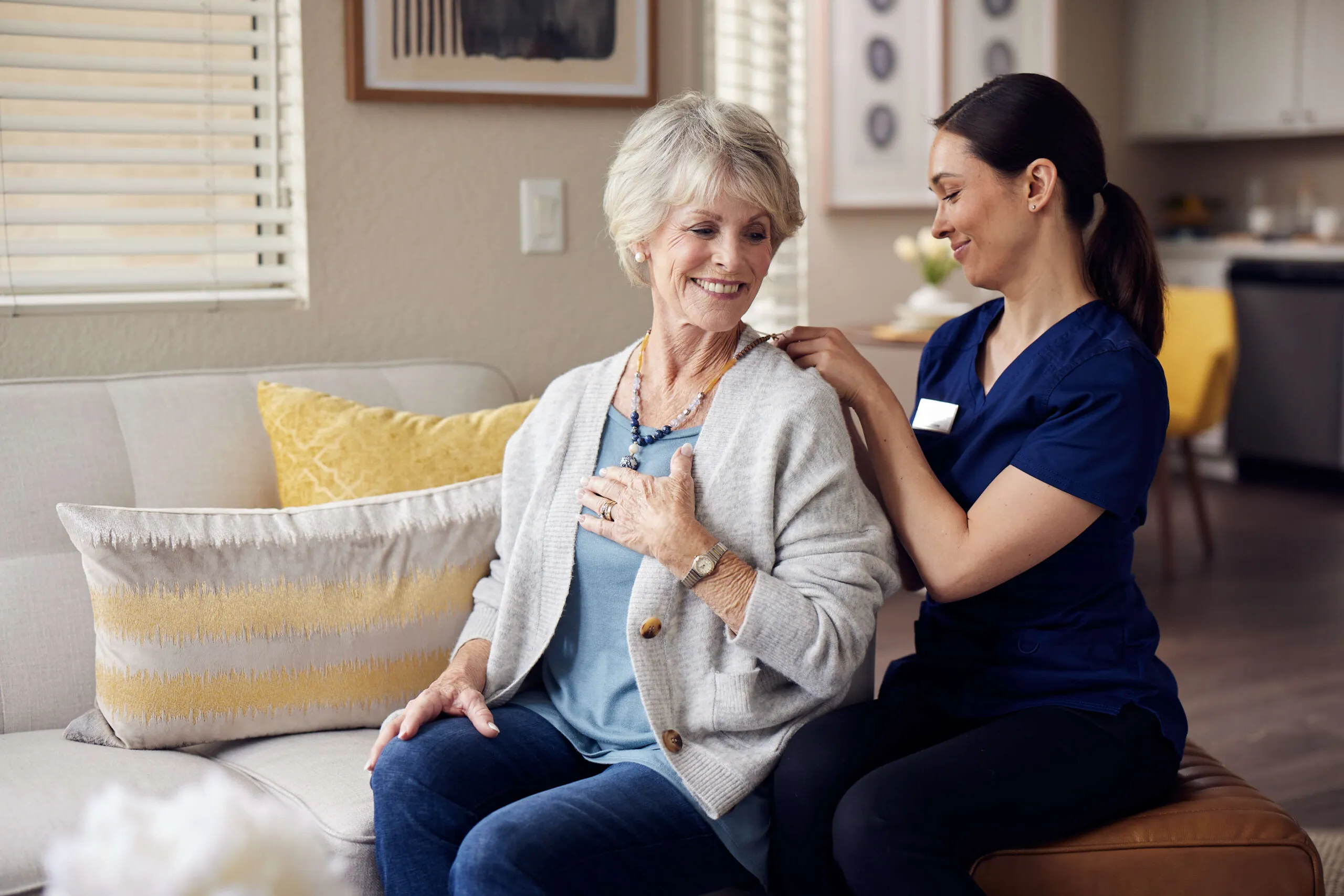 A caregiver helping an elderly woman put on her necklace.