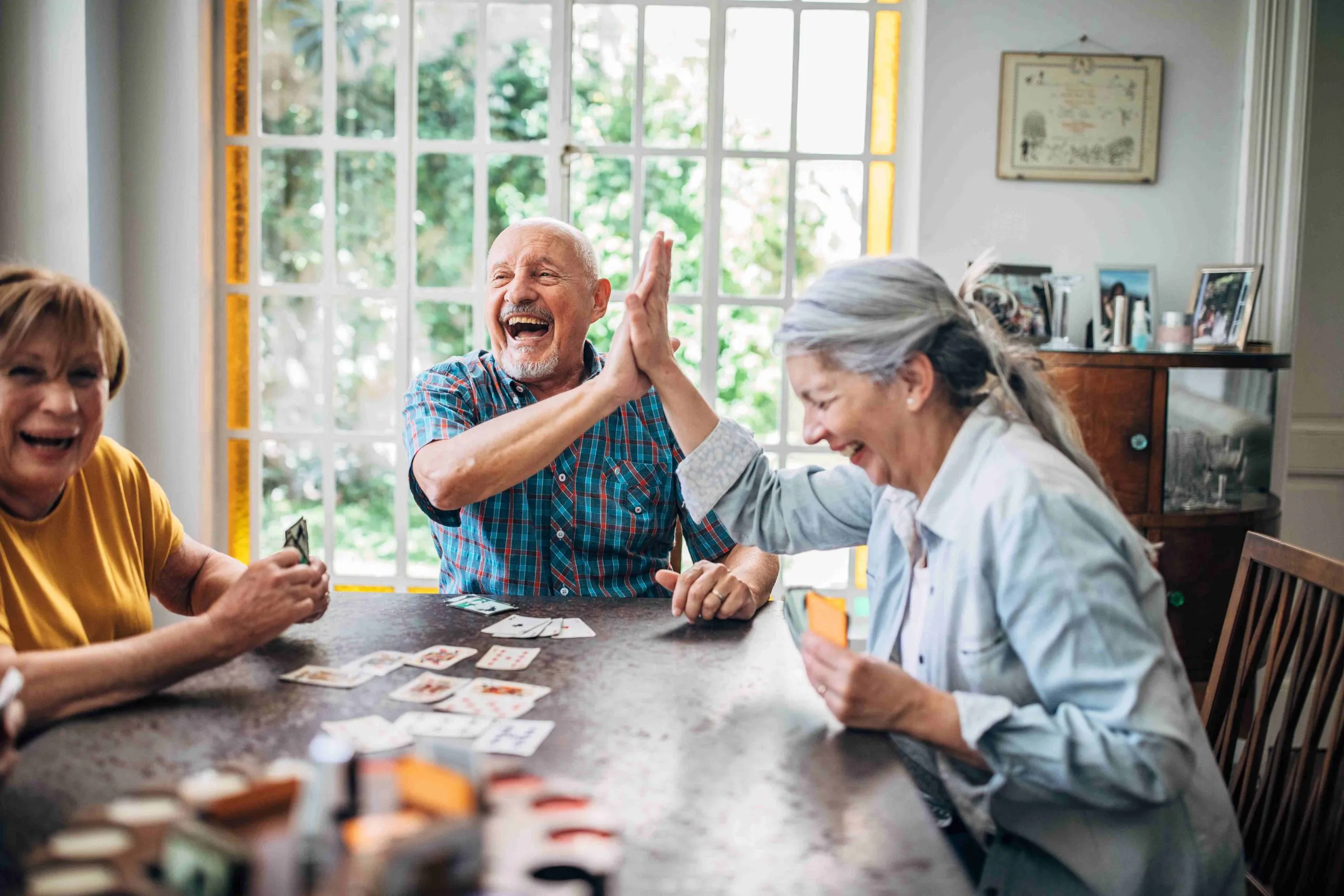 Seniors smiling and high-fiving as they play cards together.