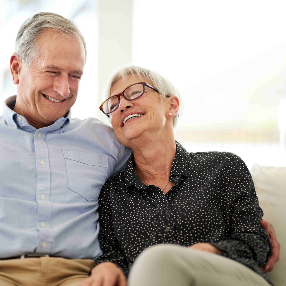 Senior couple smiling, sitting beside each other on a couch