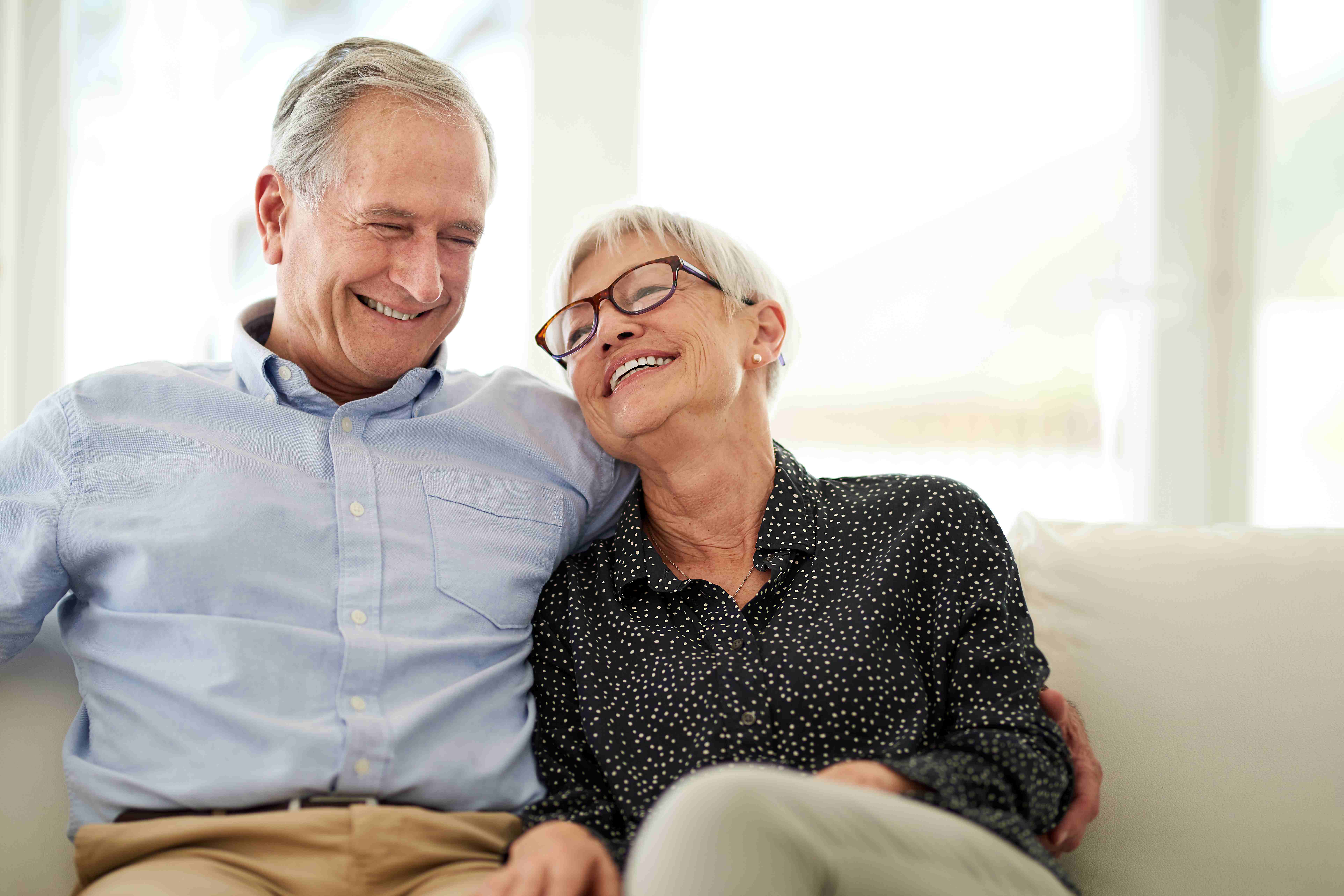 Senior couple smiling, sitting beside each other on a couch