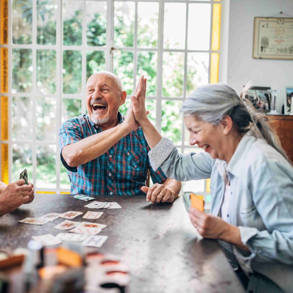 Seniors smiling and high-fiving as they play cards together.