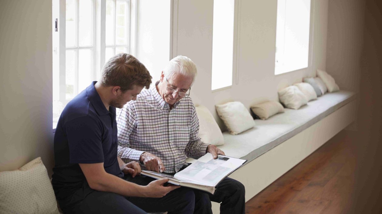 Caregiver and senior man looking at a photo album together.