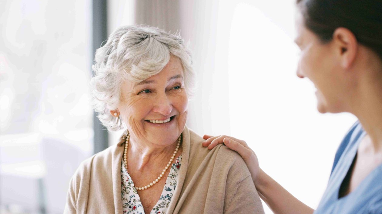 Senior woman smiling at a caregiver, with her hand on her shoulder