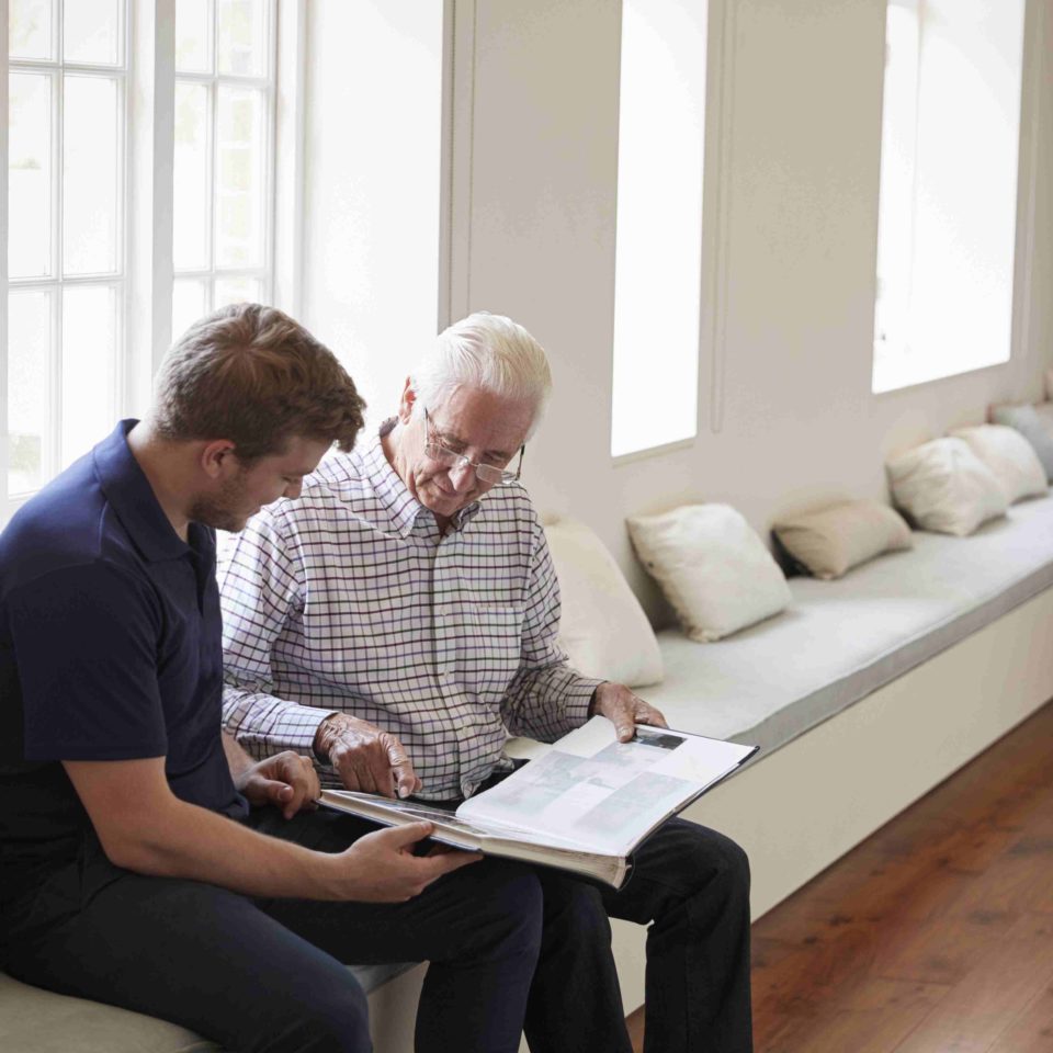 Caregiver and senior man looking at a photo album together.