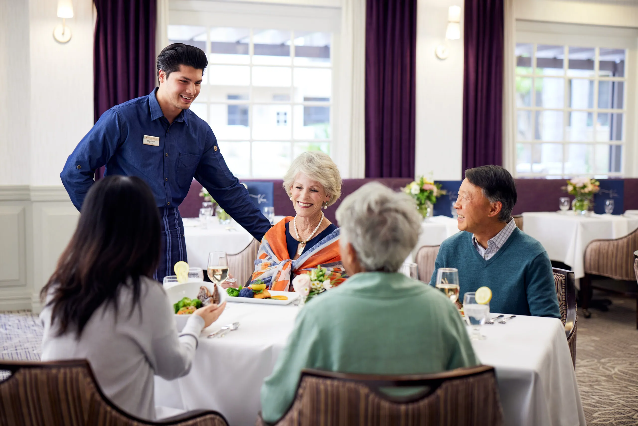 caregiver-talking-to-4-sitted-senior-people-dining