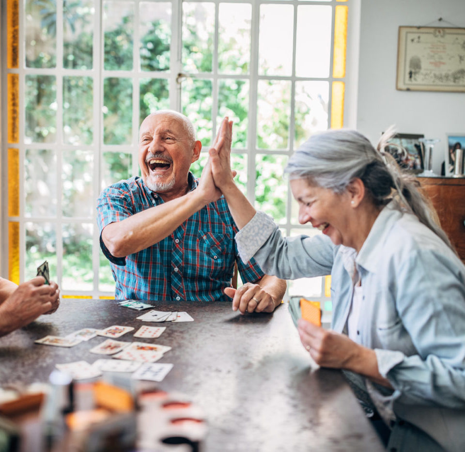 Seniors smiling and high-fiving as they play cards together.