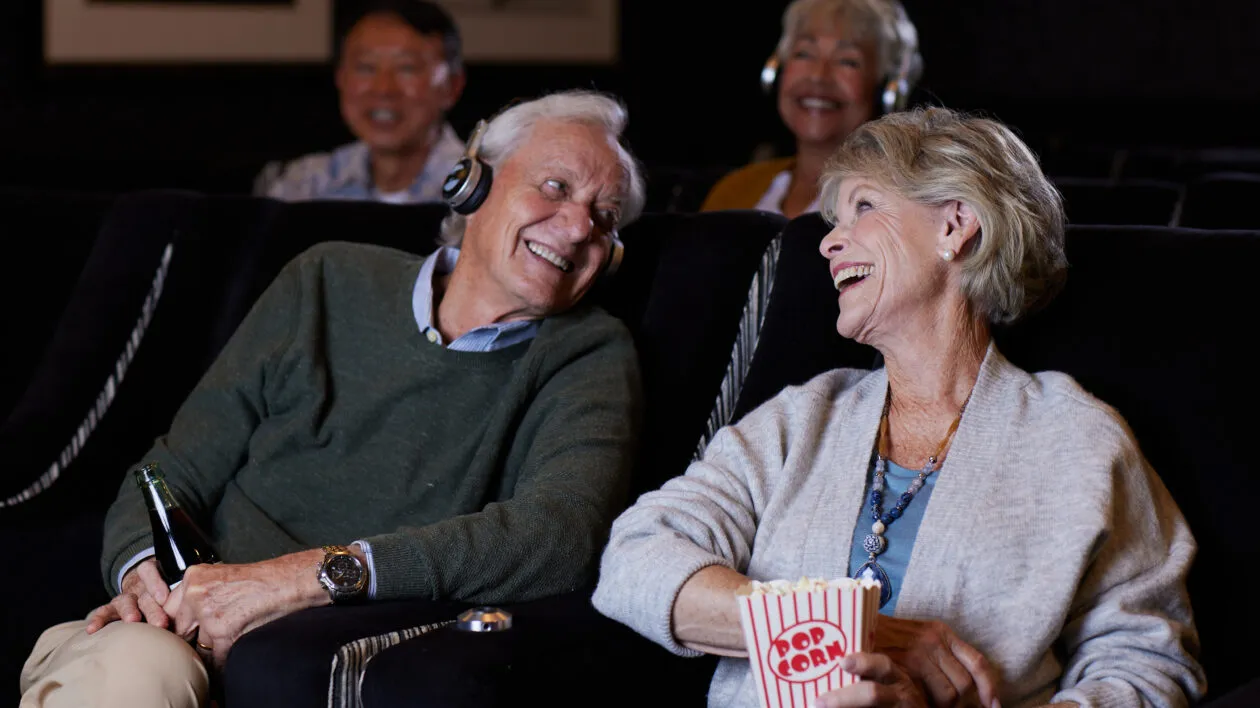 senior-couple-looking-at-each-other-at-movie-theater-with-headphones-and-popcorn