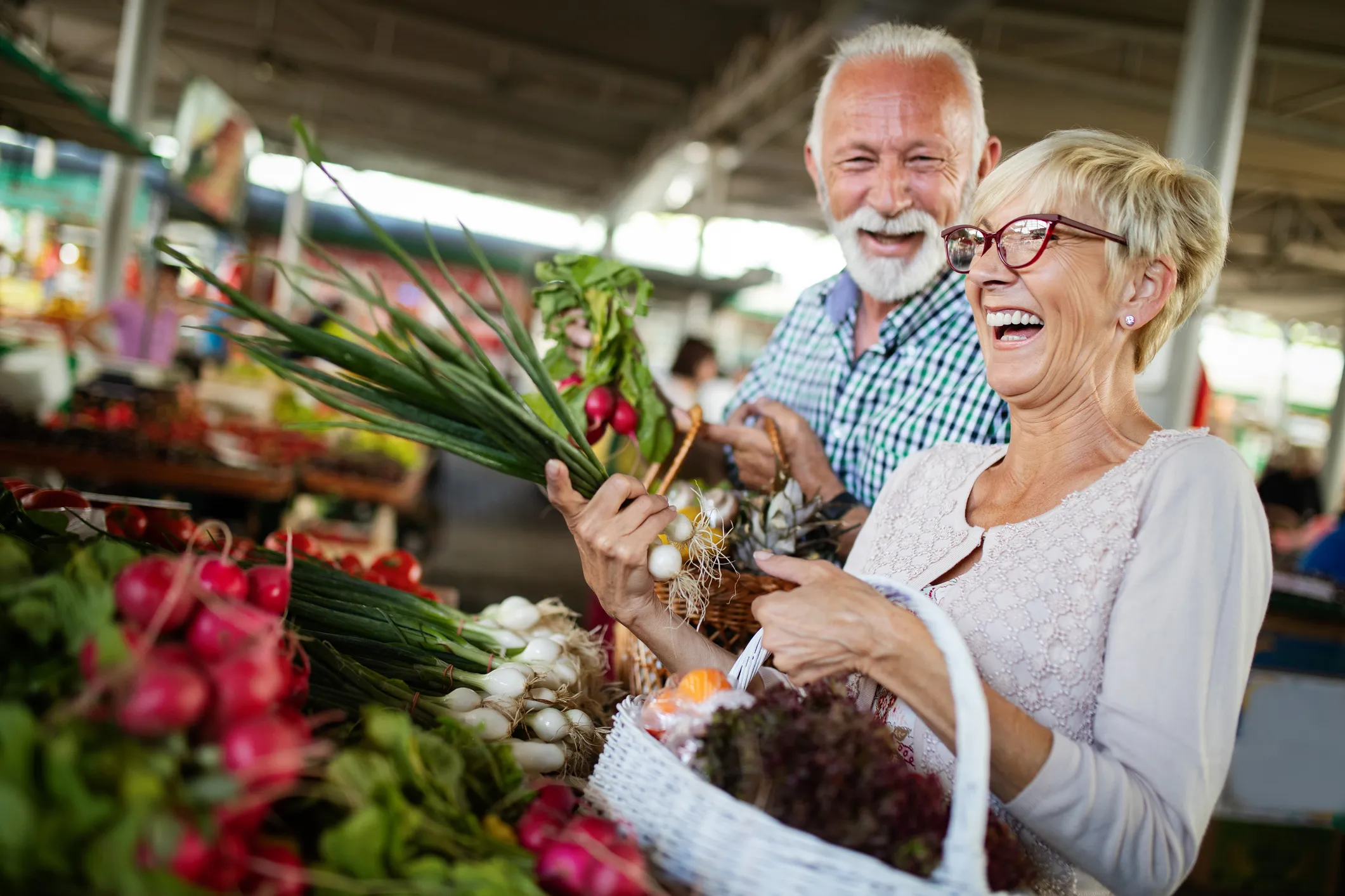 Smiling-senior-couple-holding-basket-with vegetables-at-the-market