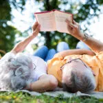 senior-couple-lying-down-reading-book-together-in-a-park