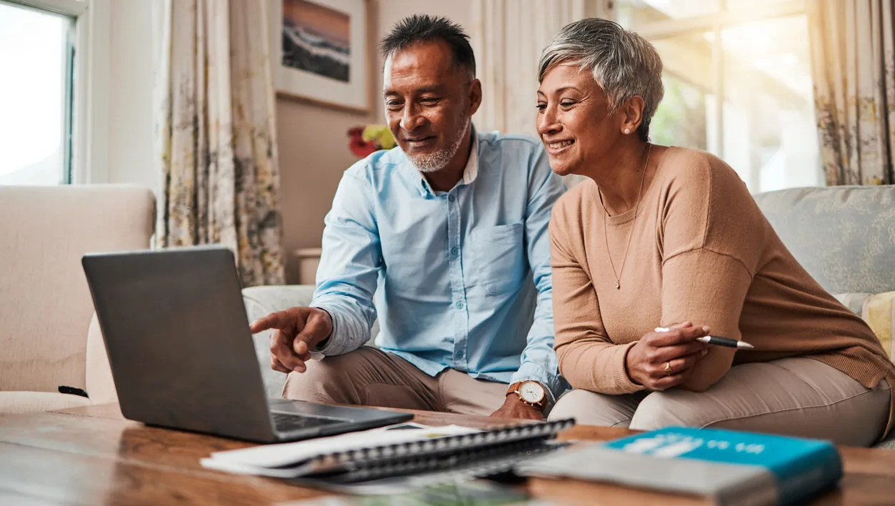 Mature couple on sofa using laptop at home for retirement planning, investment, and senior living finances.
